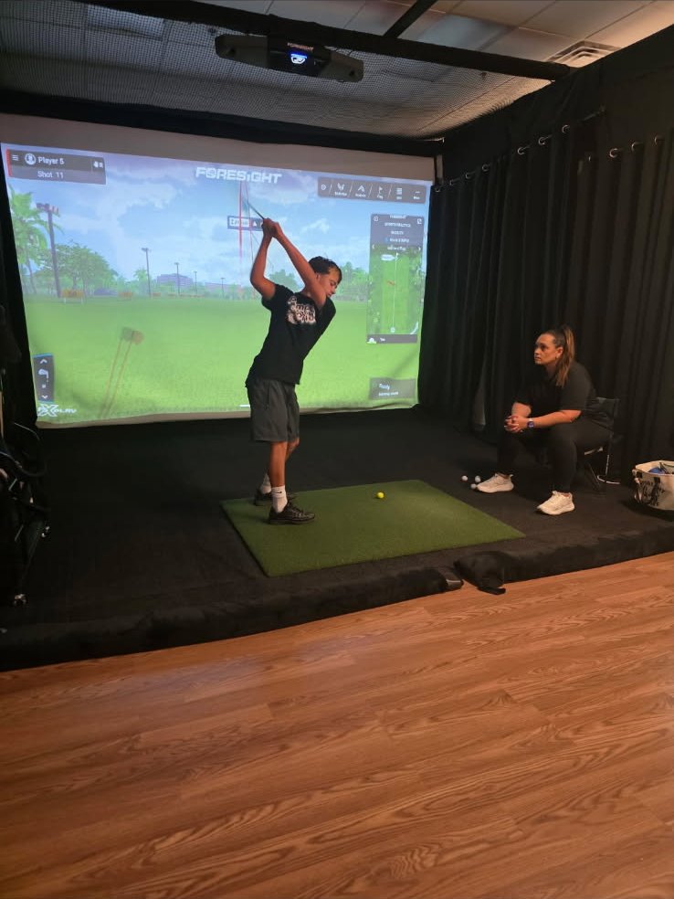 A junior golfer at the top of the backswing with Jennifer Sweet-Lopez watching at No Bogeys Bakersfield